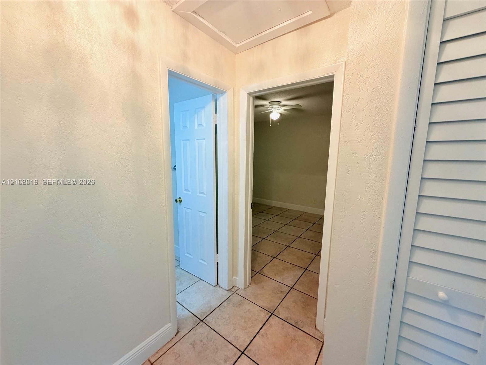Hallway featuring ceramic tile flooring, six-panel interior doors, and louvered closet doors