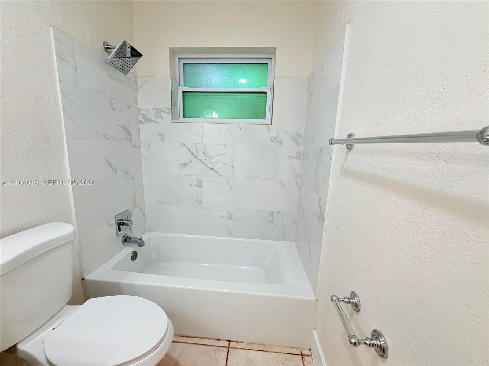 Bathtub surround featuring large-format light-toned tile, polished chrome rainfall shower head, integrated wall-mounted faucet, and polished chrome towel hardware