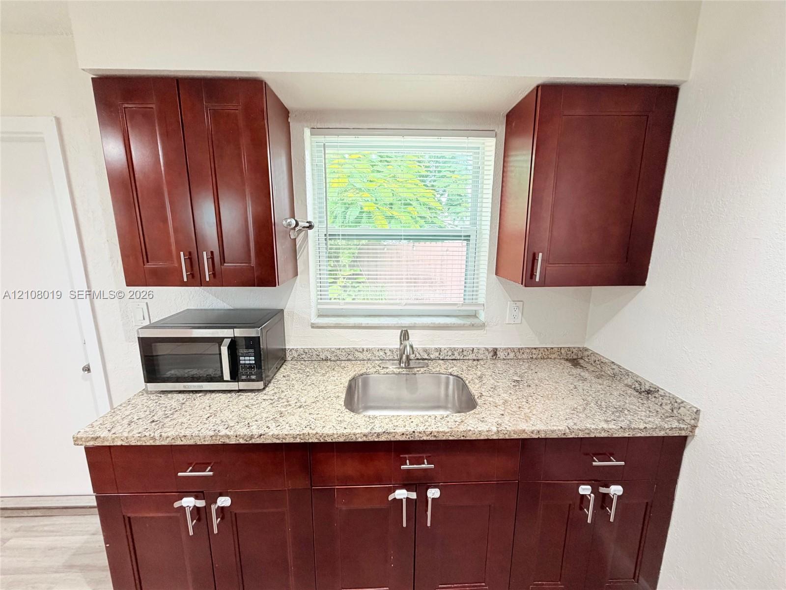 Kitchen featuring dark wood-finish cabinetry, stone-finish countertops, stainless steel undermount sink, and a high-arch faucet