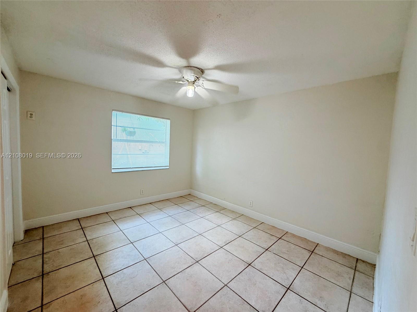 Neutral-toned room featuring tiled flooring, a single window, and a ceiling fan with integrated lighting