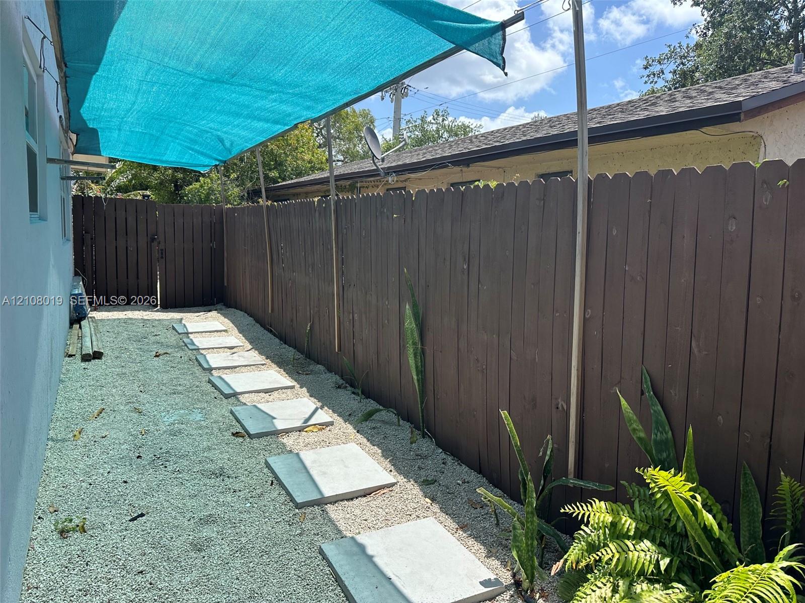 Side yard featuring a privacy fence, stone paver walkway, gravel ground cover, and a sun shade canopy