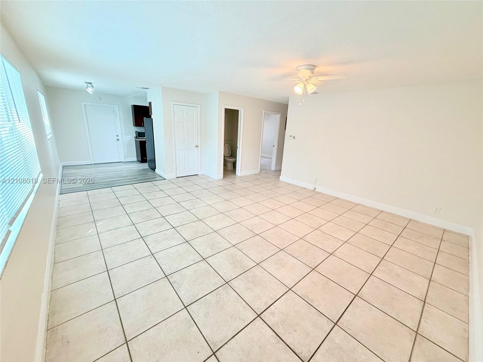 Neutral-toned interior featuring large-format square tile flooring, a ceiling-mounted light fixture with fan, and multi-pane horizontal blinds