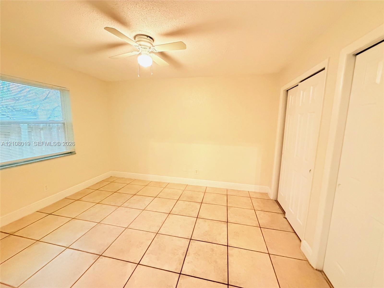 Tile flooring, white bi-fold closet doors, and a ceiling fan with integrated lighting