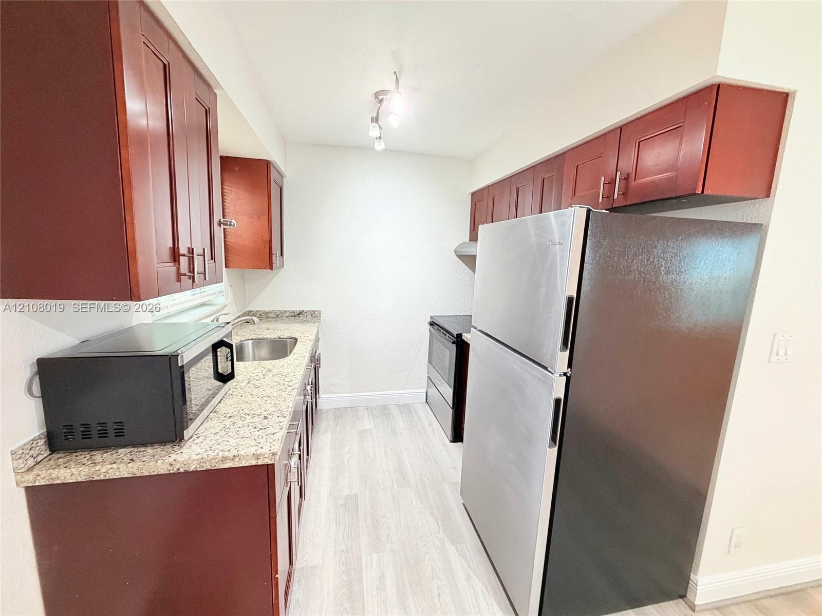 Kitchen featuring wood-finish cabinetry, stone-surface countertops, stainless steel refrigerator, integrated range, and recessed ceiling lighting