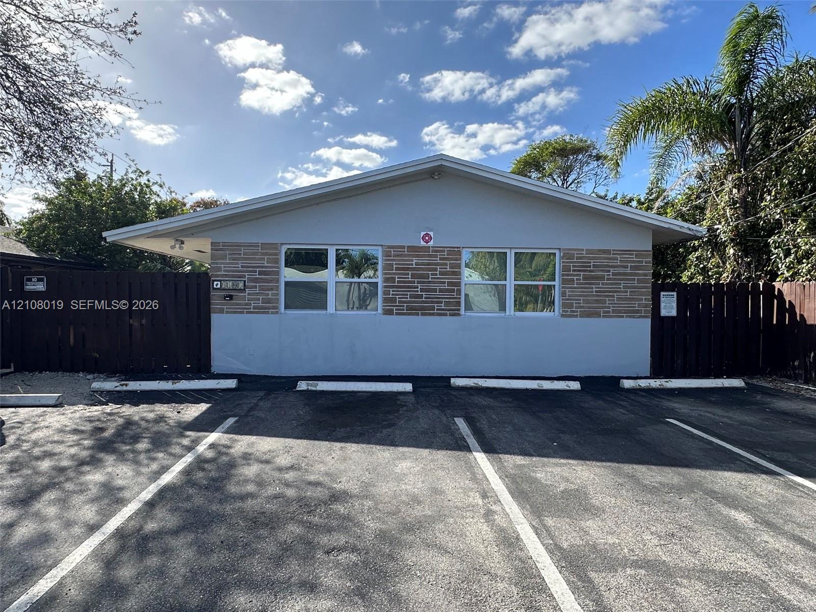 Exterior facade featuring stone veneer detailing, wide-eave roofline, and dedicated parking spaces bordered by privacy fencing