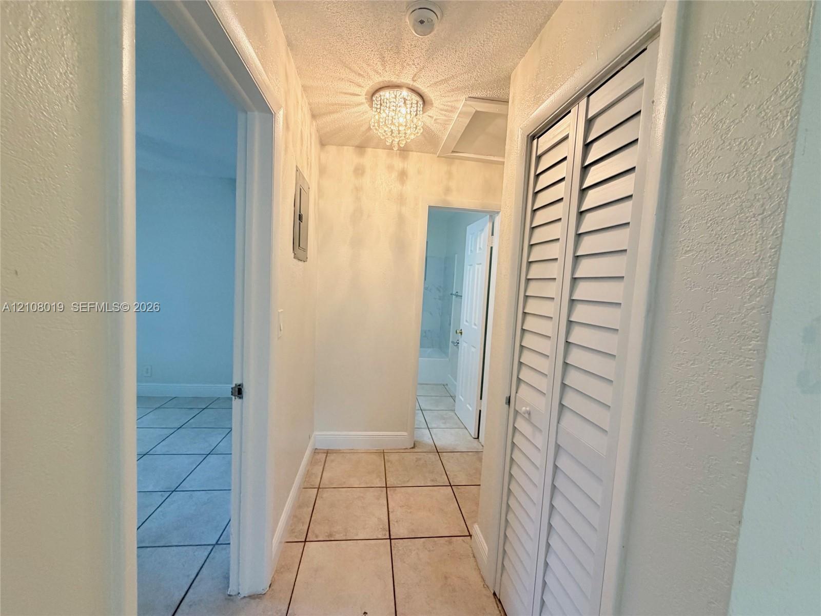 Hallway featuring ceramic tile flooring, a crystal-style flush mount light fixture, and white louvered-panel closet doors