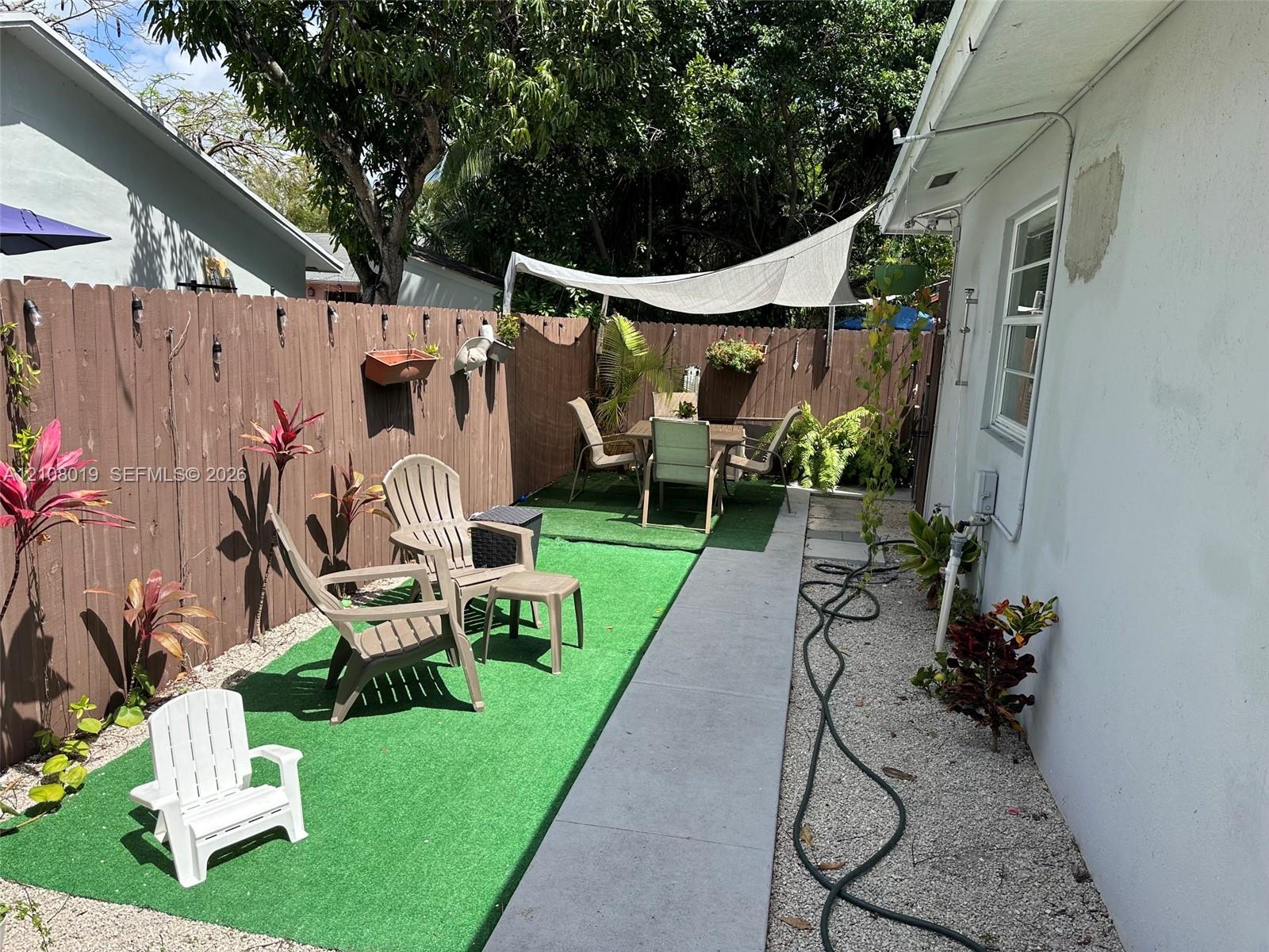 Private outdoor space featuring a wood-panel fence, synthetic grass, concrete walkway, and gravel ground cover