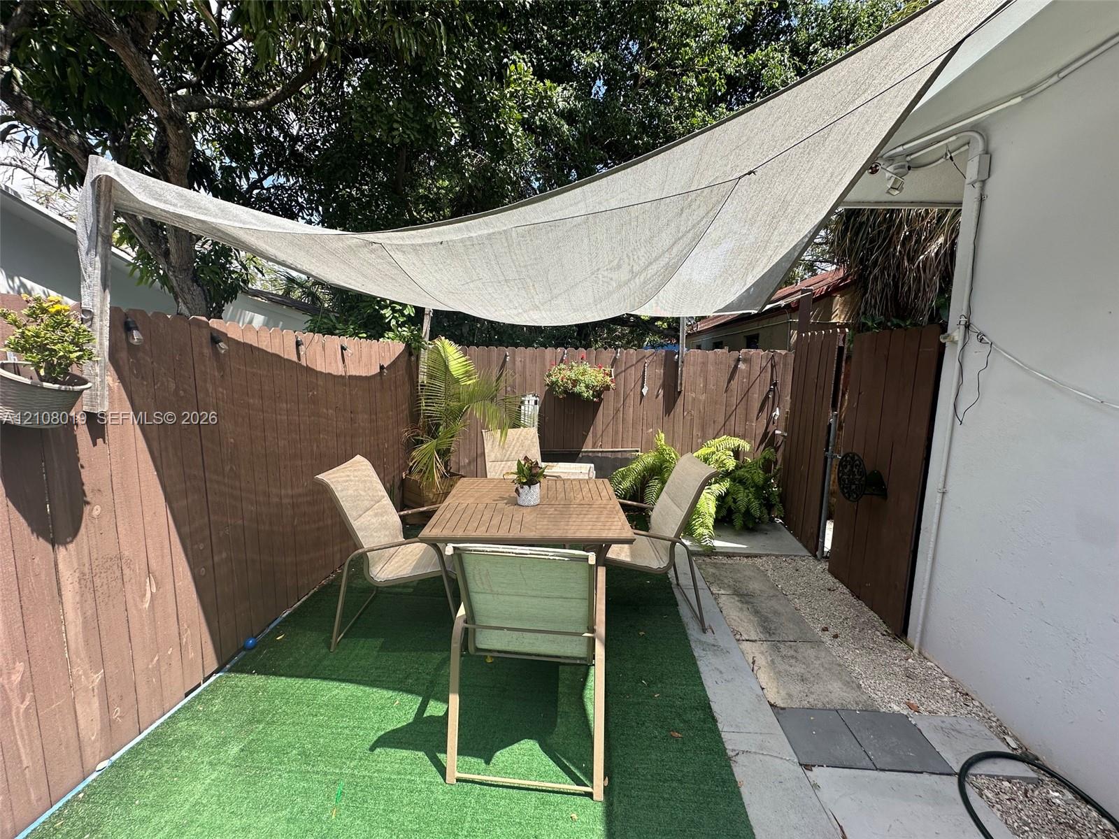 Enclosed patio area featuring a vertical wood fence, artificial turf surfacing, and an overhead tensioned sun shade sail
