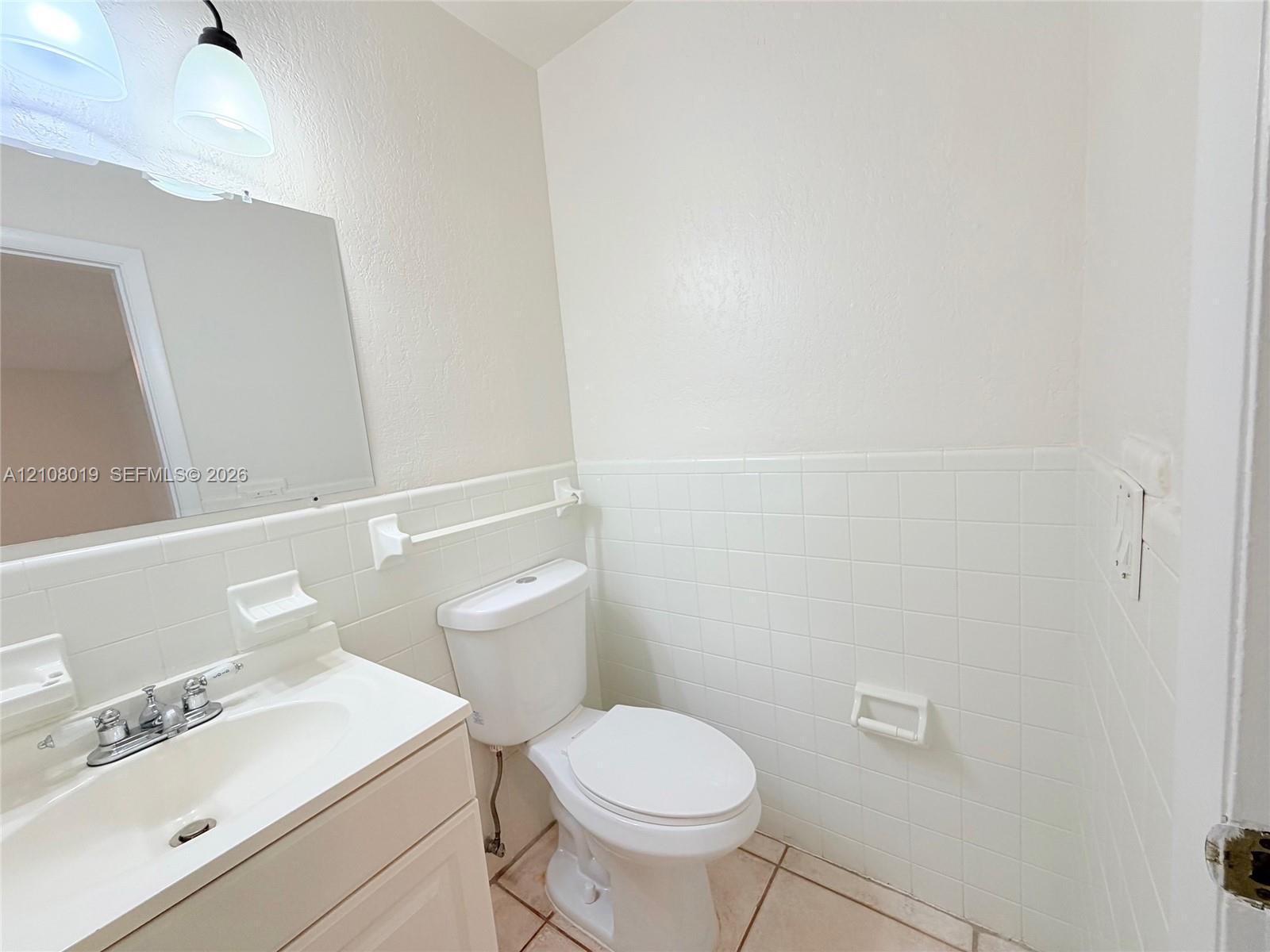 Bathroom featuring a vanity with an integrated sink, polished chrome widespread faucet, wall-mounted mirror, ceramic tile wainscoting, and ceramic floor tiling