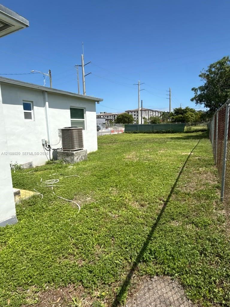 Exterior lot space featuring a grass-covered yard, chain-link perimeter fencing, and an external HVAC unit