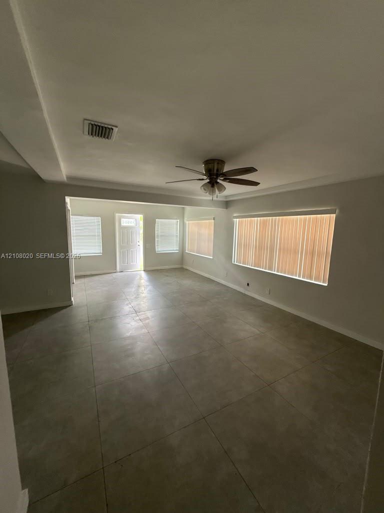Neutral-toned tile flooring, recessed ceiling design, ceiling fan with integrated lighting, and multiple windows with vertical blinds