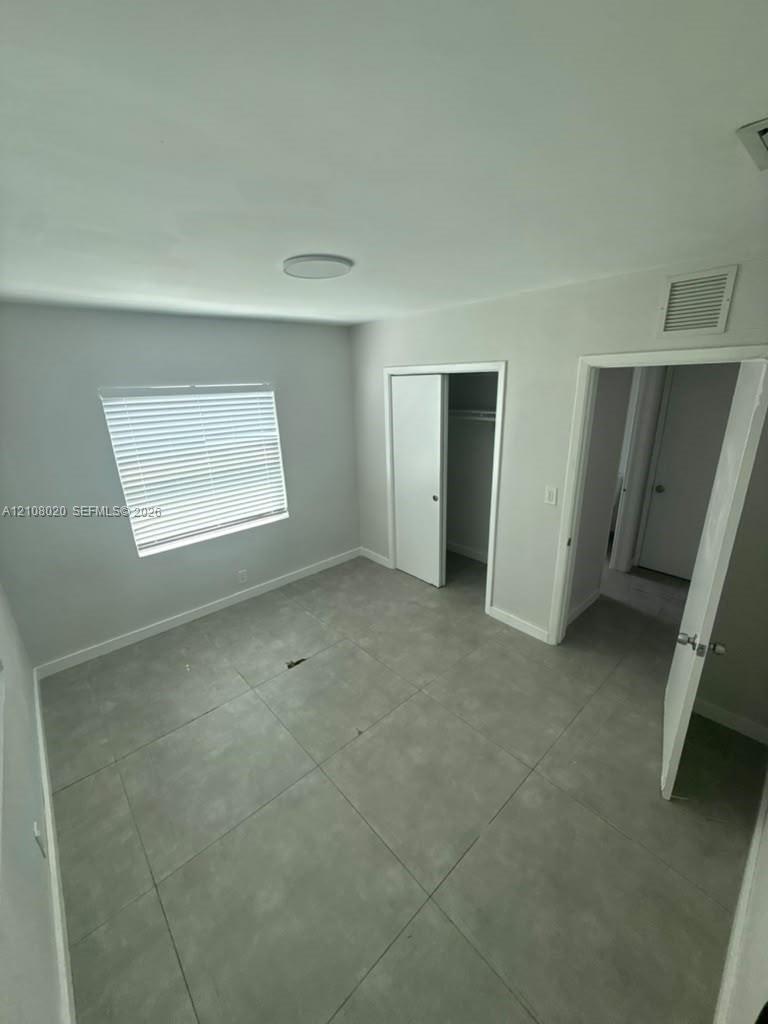 Large-format neutral tile flooring, window with installed blinds, and built-in closet storage