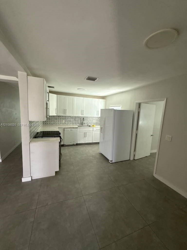 Kitchen featuring white shaker-style cabinetry, patterned tile backsplash, large-format tile flooring, and white built-in appliances
