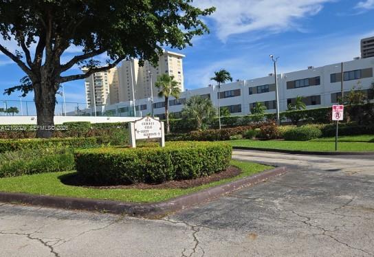 Landscaped grounds featuring manicured hedging, mature trees, paved driveways, and exterior building facades
