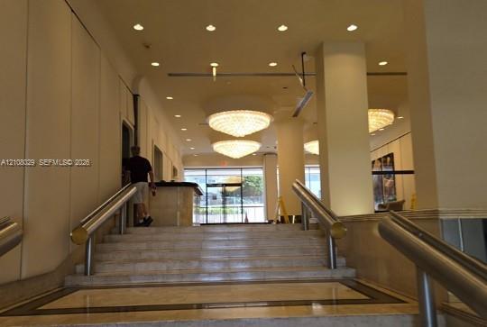 Entryway featuring stone steps, dual metallic handrails, recessed ceiling lighting, and tiered crystal chandeliers