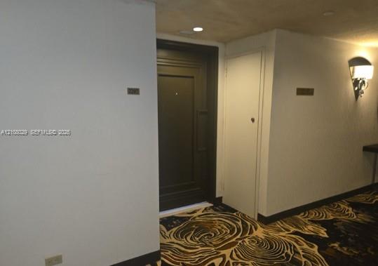 Entryway featuring a dark-finish panel door, recessed ceiling lighting, wall-mounted light fixture, and patterned carpet flooring