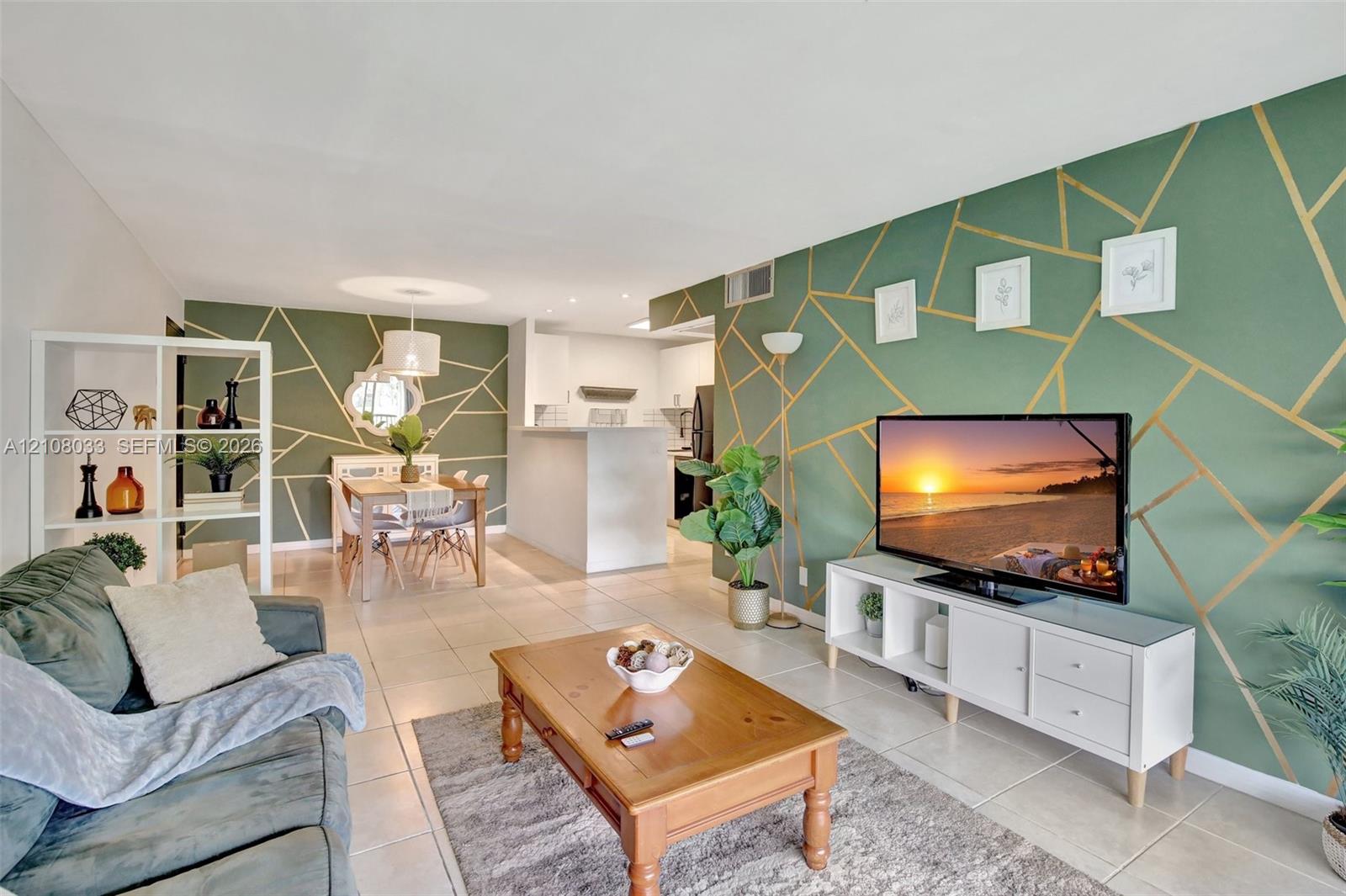 Open-concept floor plan featuring large-format ceramic tile flooring, accent walls with geometric gold detailing, and a kitchen peninsula
