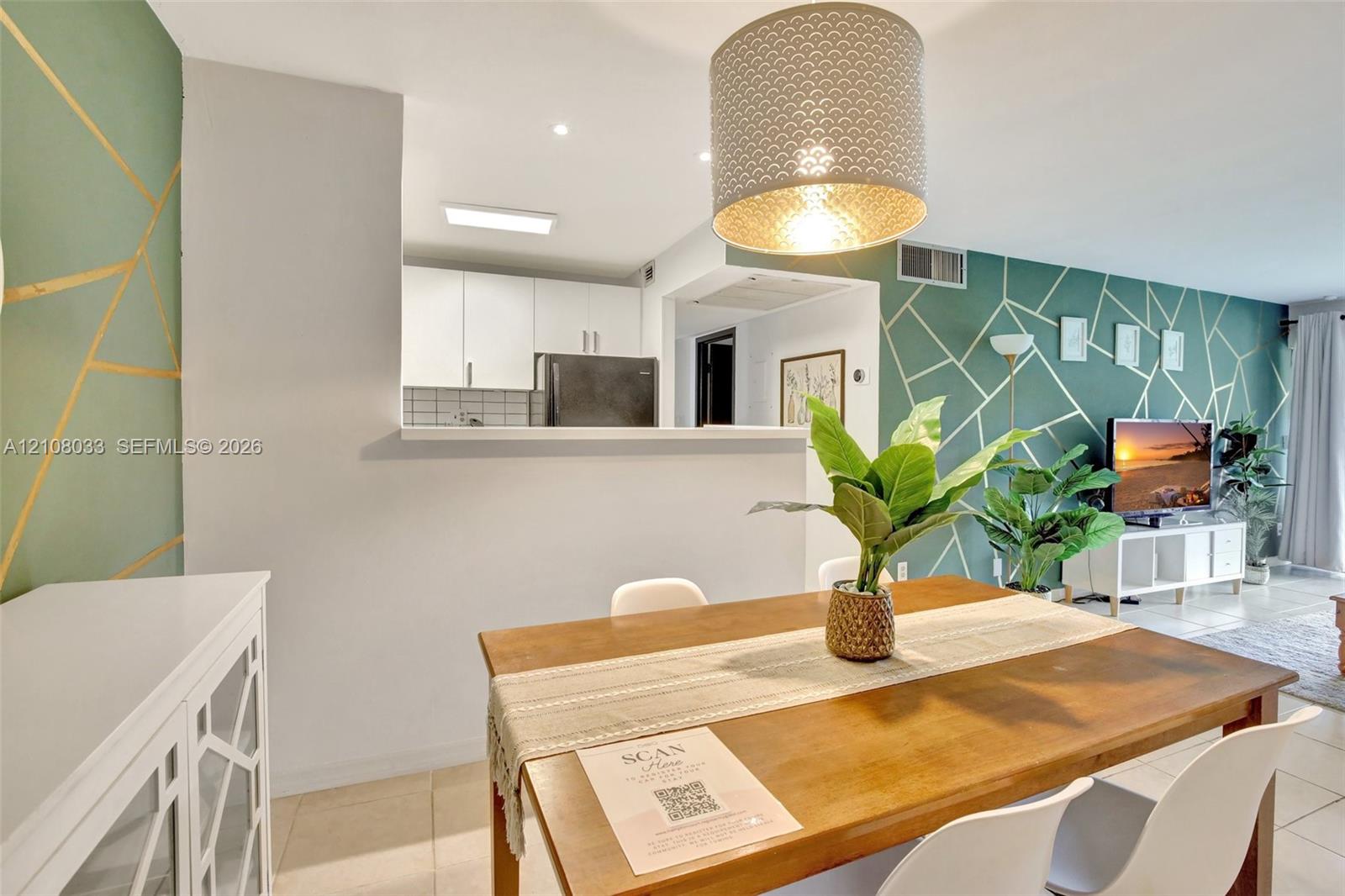 Open-concept interior featuring geometric accent walls, pass-through kitchen opening, drum pendant lighting, and large-format tile flooring