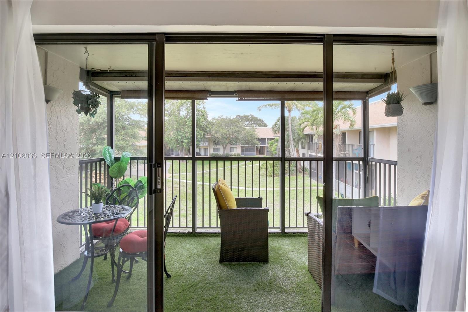 Screened-in balcony featuring an overhead cover, synthetic turf flooring, and metal railing