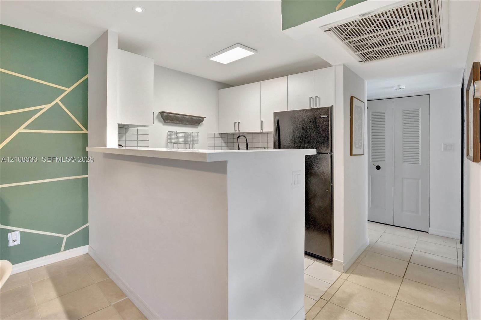 Kitchen featuring a breakfast bar, white cabinetry, tile backsplash, black refrigerator, and tile flooring