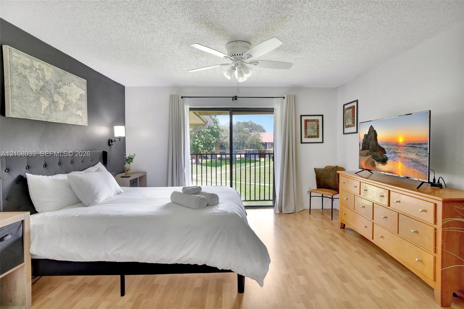 Wood-finish flooring, accent wall, ceiling fan with integrated lighting, and glass sliding door featuring a metal railing