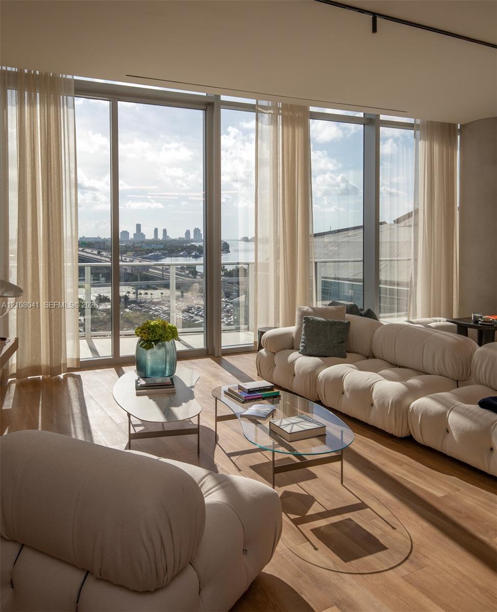 Floor-to-ceiling glass windows, wide-plank wood-finish flooring, metal-framed balcony access, and track lighting