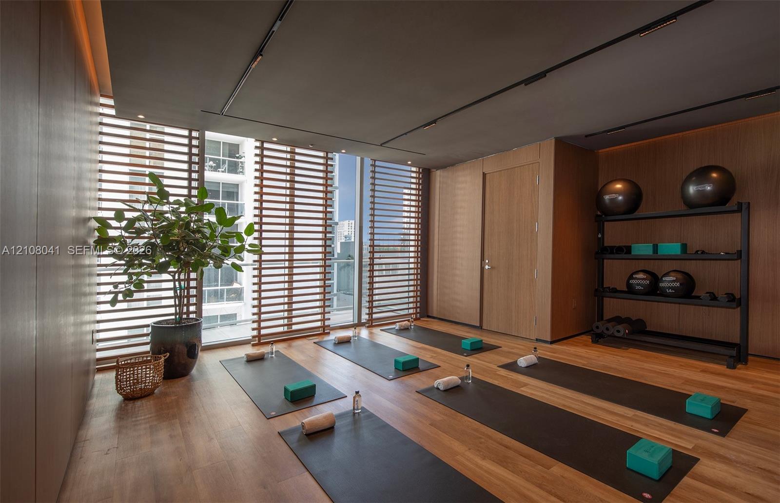 Wood-finish flooring, floor-to-ceiling windows with horizontal wood-slat privacy screens, recessed ceiling track lighting, and full-wall wood paneling