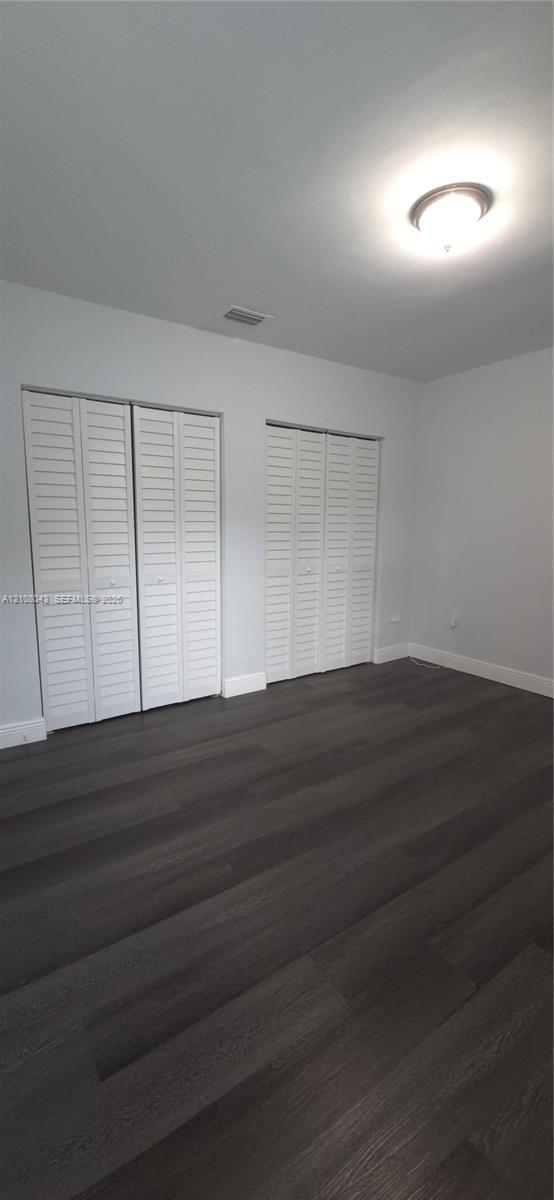Room featuring wood-finish flooring, two sets of white louvered-door closets, and a central flush-mount ceiling light fixture