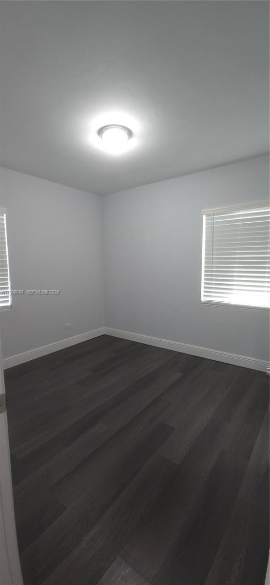 Neutral-toned interior featuring wood-finish flooring, white walls, two windows with horizontal blinds, and a flush-mount ceiling light fixture
