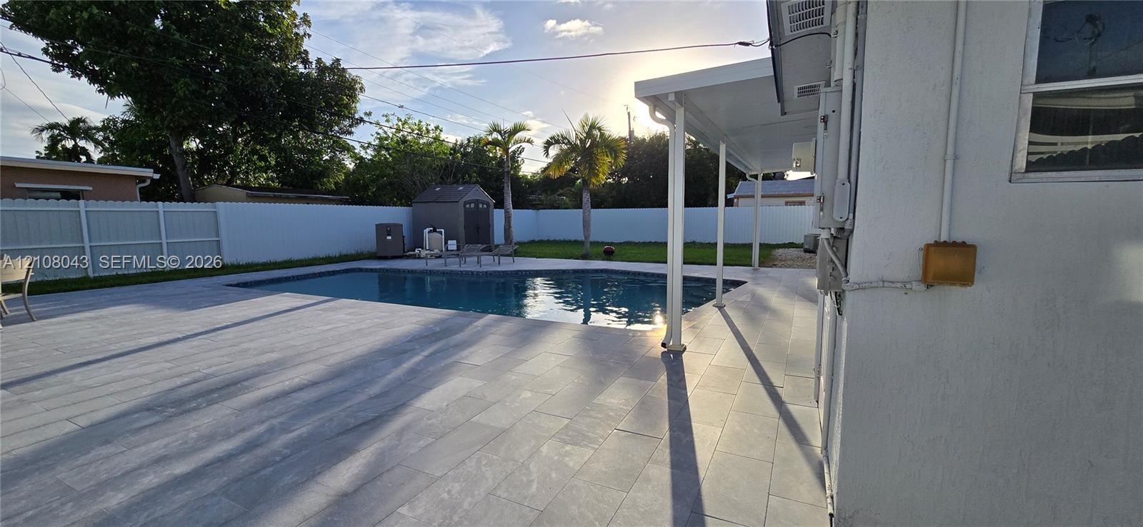 Backyard featuring a concrete-tiled patio, in-ground swimming pool, covered lanai, and white vinyl privacy fencing