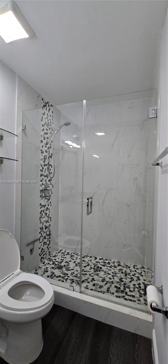 Walk-in shower featuring a frameless glass door, stone-finish mosaic floor tile, accent tile wall detail, and chrome shower fixtures