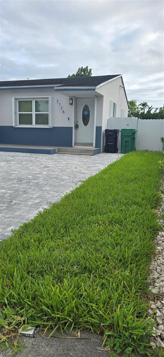 Exterior elevation featuring a two-tone stucco facade, paver driveway, front entrance with an oval-glass door, and vinyl privacy fencing