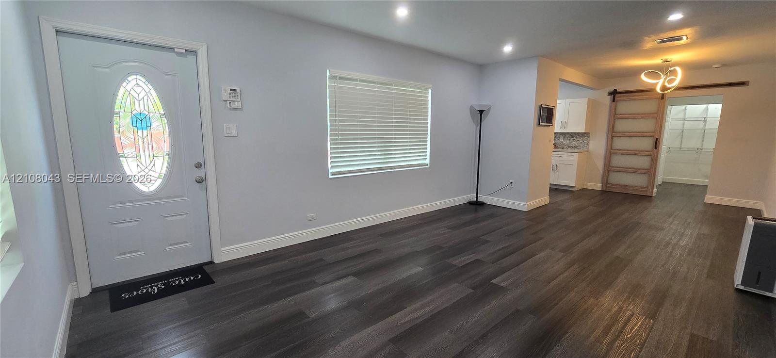 Interior featuring wood-finish flooring, recessed lighting, an oval-glass paneled entry door, a sliding barn-style door, and built-in white cabinetry