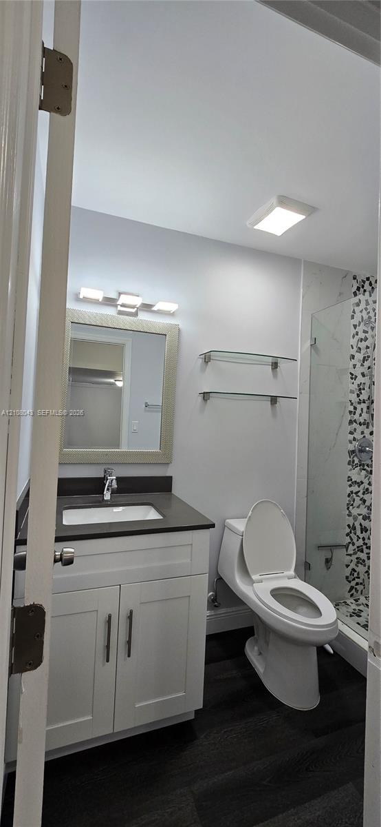 Bathroom featuring a white shaker-style vanity with a dark countertop, undermount sink, glass wall-mounted shelving, and wood-finish flooring