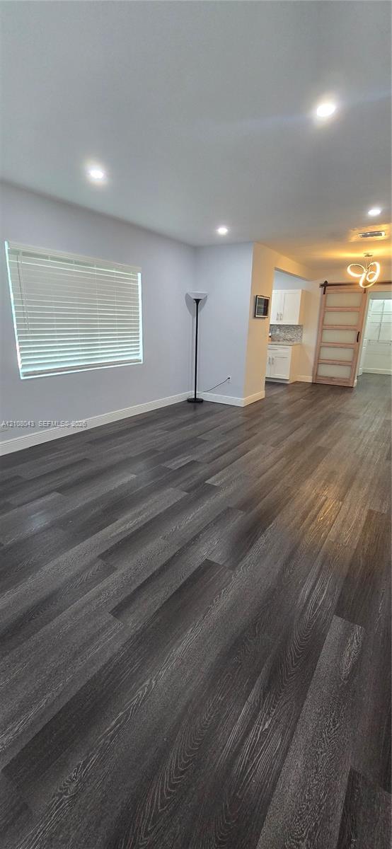 Open-concept room featuring wood-finish flooring, recessed lighting, horizontal window blinds, and a sliding barn-style door