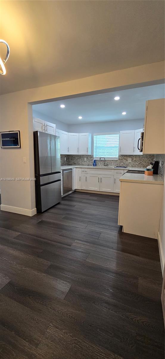 Kitchen featuring white shaker-style cabinetry, stainless steel appliances, patterned tile backsplash, recessed lighting, and wood-finish flooring