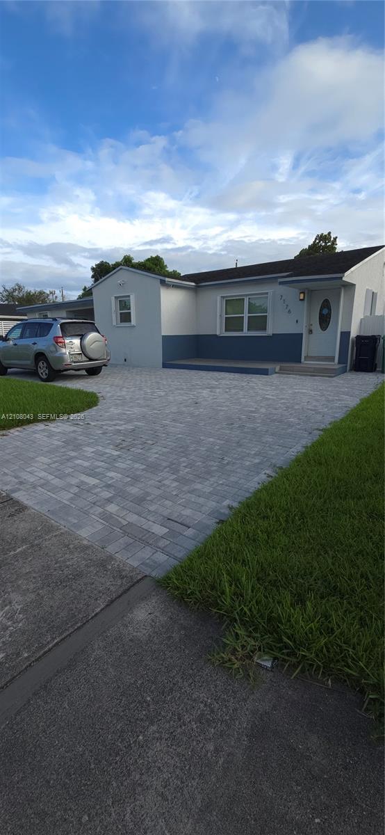 Single-story exterior featuring a two-tone smooth stucco finish, paver driveway, covered front entryway, and asphalt shingle roofing