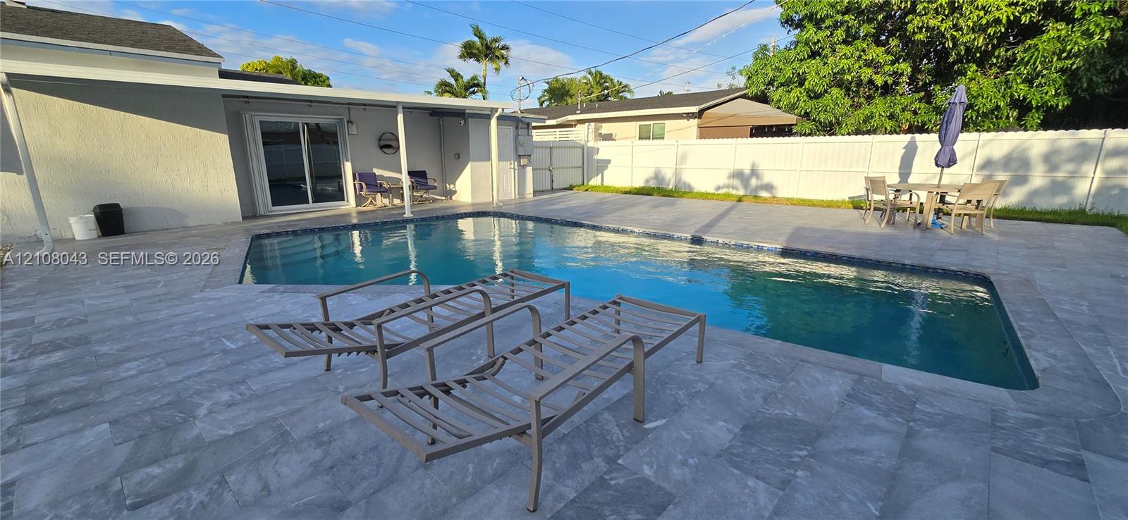 Backyard featuring a paved stone patio, an in-ground swimming pool with tile trim, a covered exterior area, and a white vinyl perimeter fence