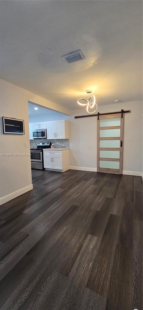 Wood-finish flooring, sliding barn door with frosted glass panels, modern multi-ring chandelier, and white cabinetry