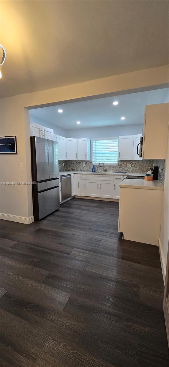 Kitchen featuring white shaker-style cabinetry, stainless steel appliances, recessed ceiling lighting, wood-finish flooring, and a patterned tile backsplash