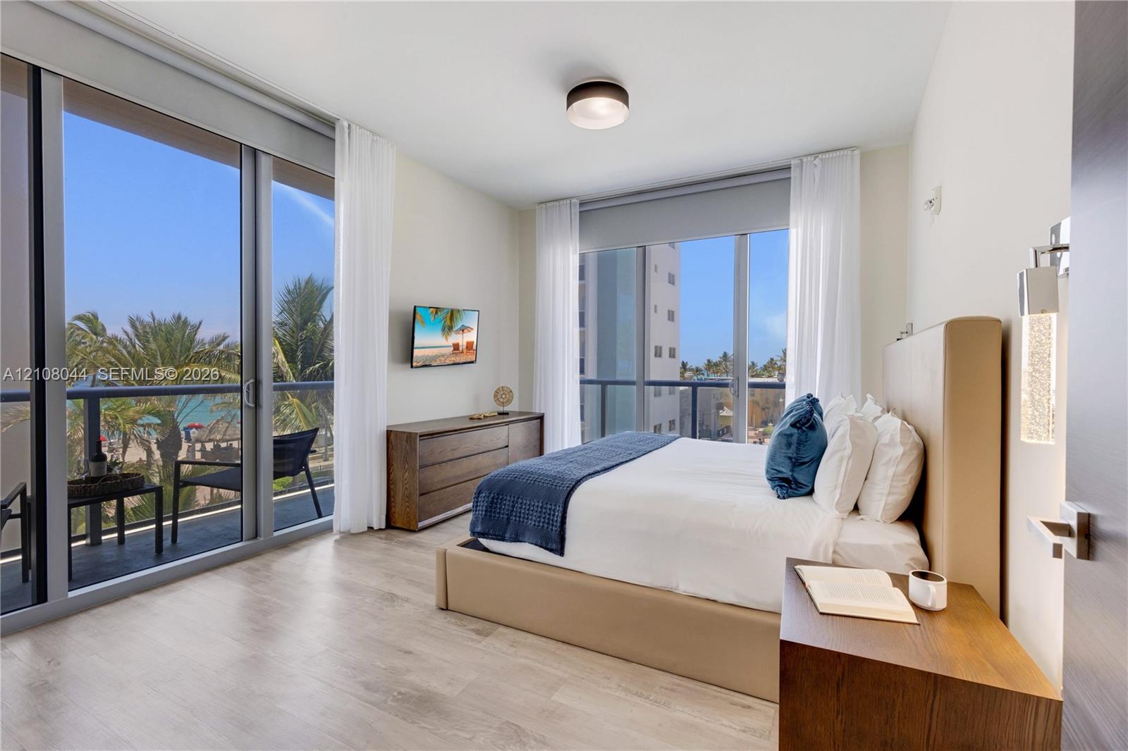 Floor-to-ceiling glass sliding doors, wood-finish flooring, private balcony with metal railing, and wall-mounted cylindrical light fixture