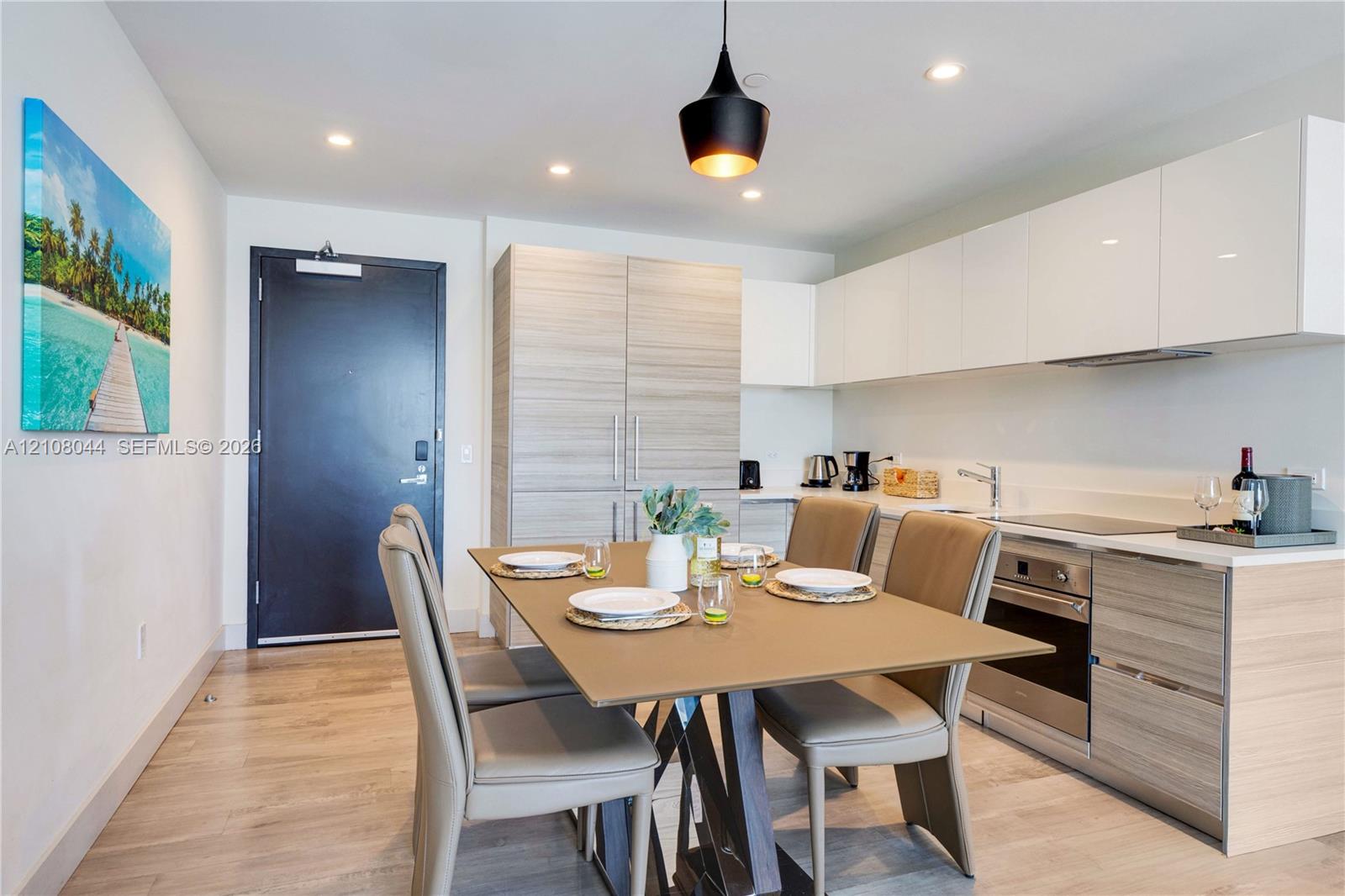 Modern kitchen featuring high-gloss white upper cabinetry, wood-finish lower cabinetry, integrated stainless steel oven, recessed lighting, and a pendant light fixture