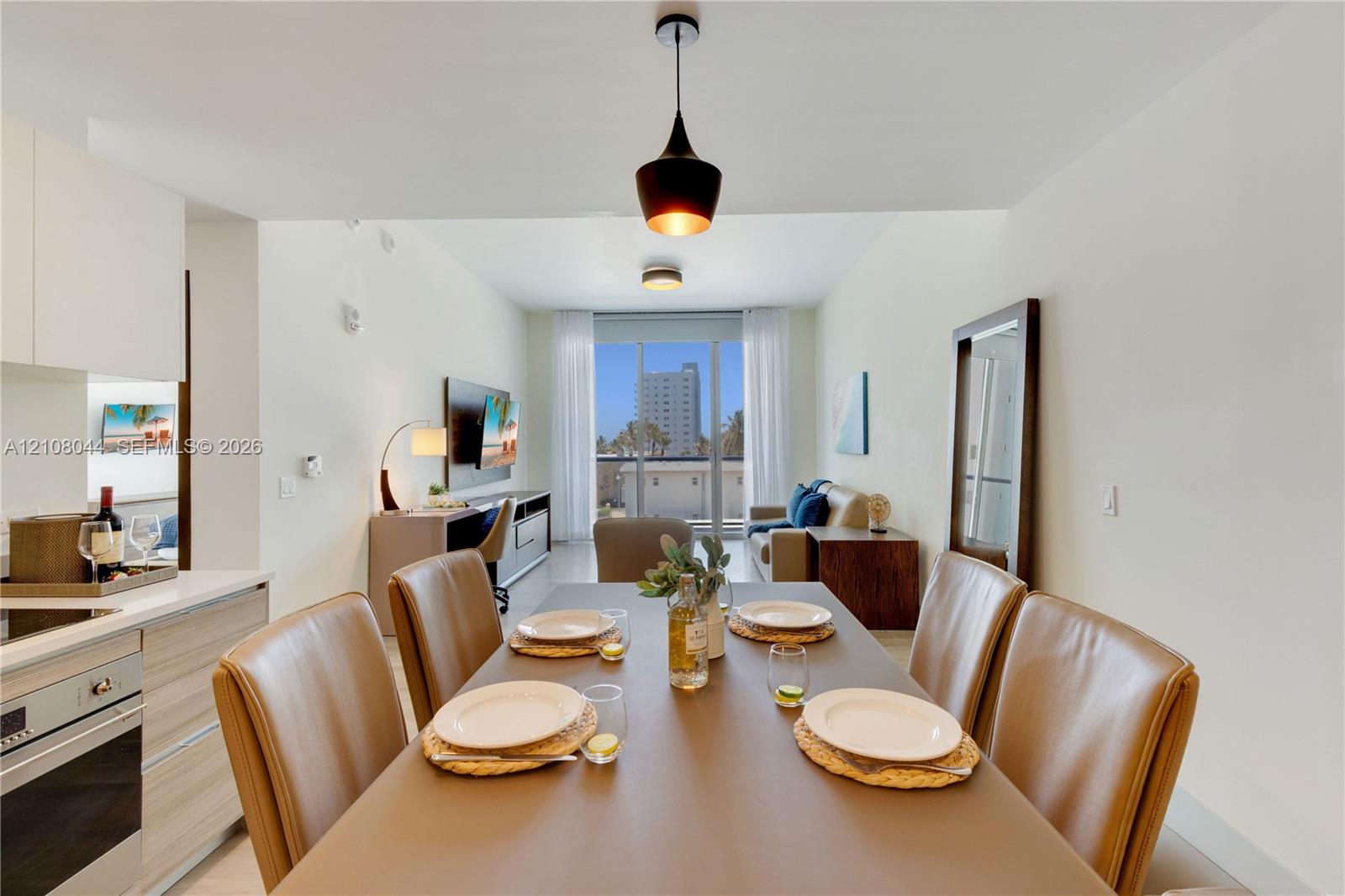 Kitchen area with built-in cabinetry, stainless steel oven, and light-toned wood-finish cabinetry, complemented by a hanging pendant light fixture and floor-to-ceiling glass doors
