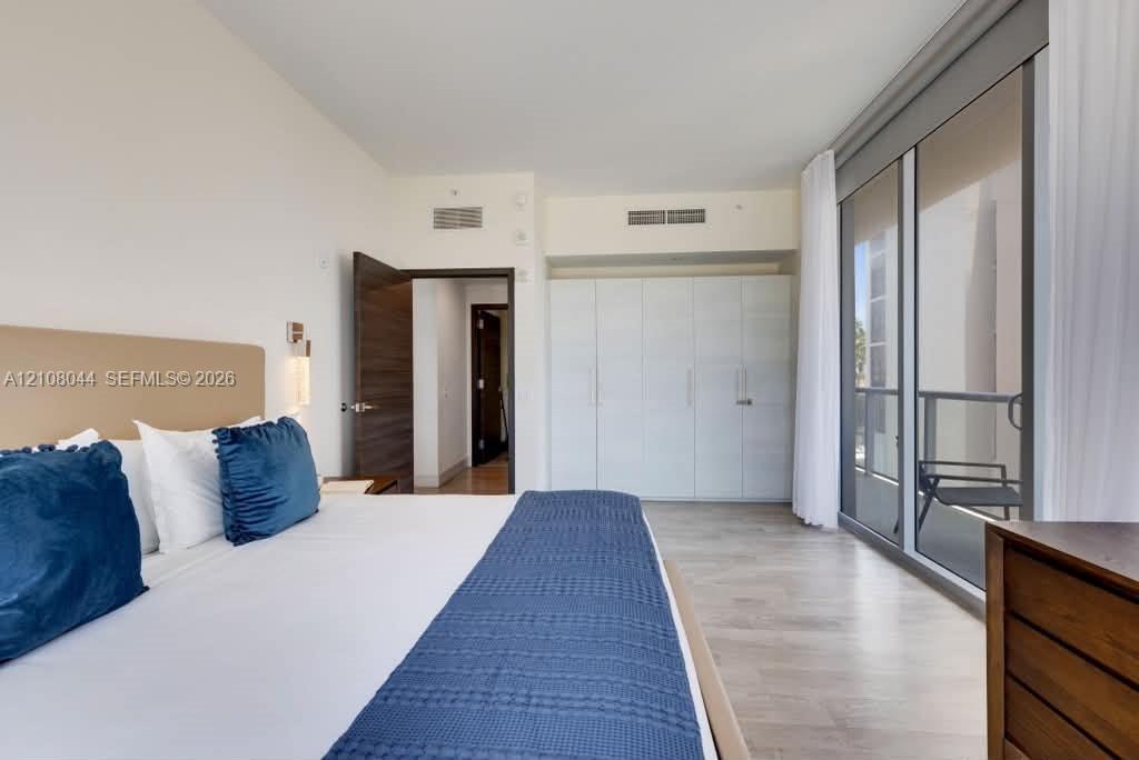 Floor-to-ceiling glass sliding doors with balcony access, wood-finish flooring, built-in floor-to-ceiling cabinetry, and solid-core interior doors