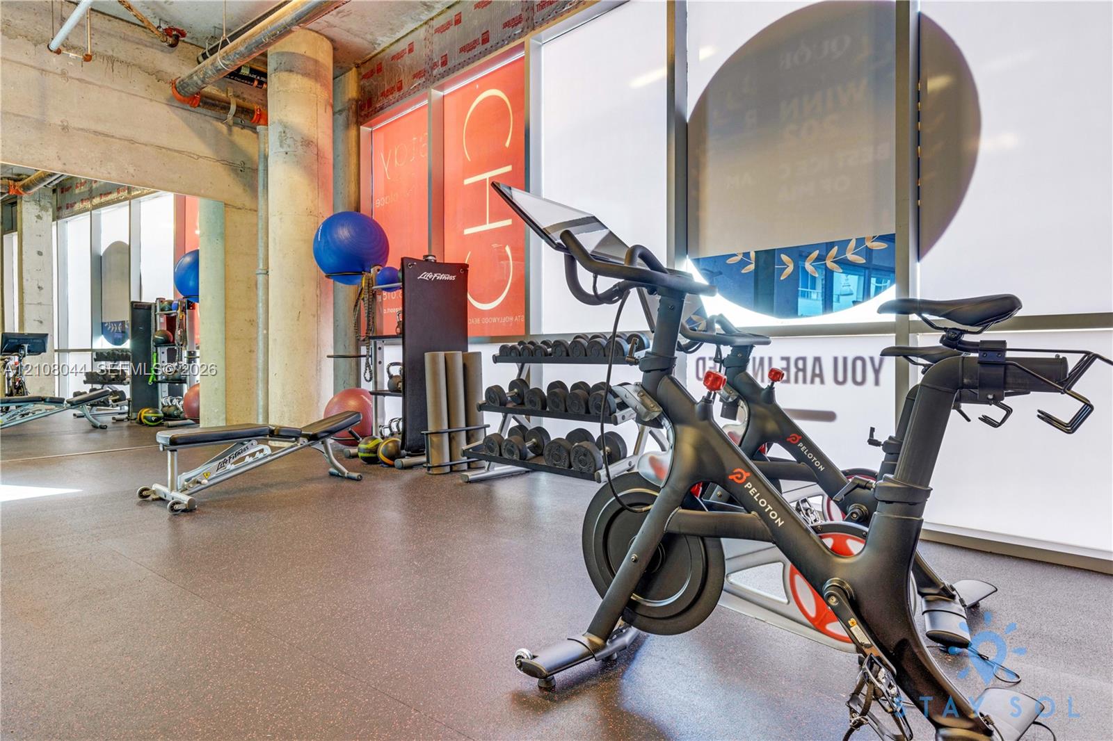 Fitness center featuring floor-to-ceiling windows, exposed concrete ceiling, industrial structural column, and resilient rubberized flooring