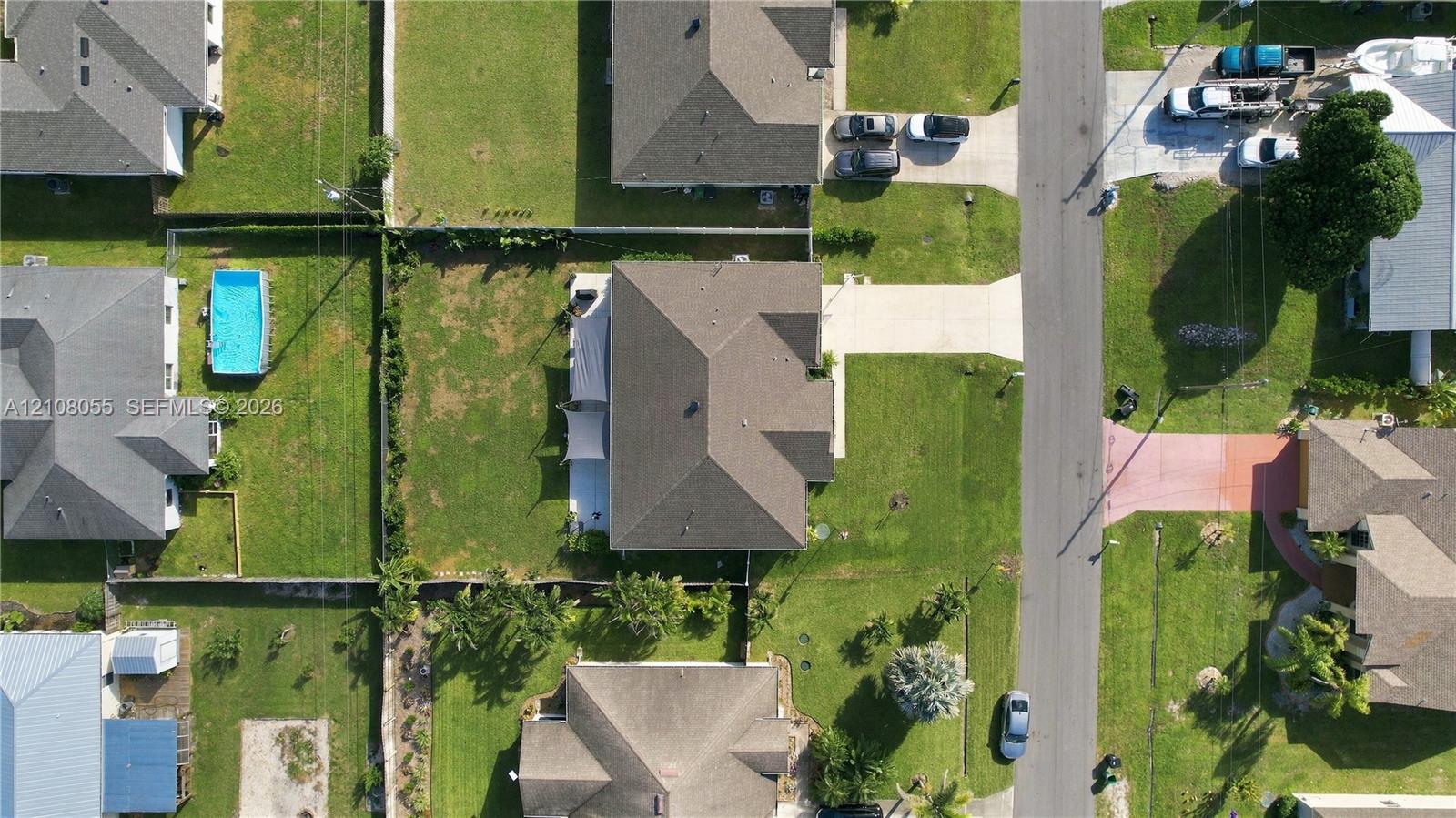 Aerial perspective of a residential property featuring a concrete driveway, a multi-faceted shingle roofline, and an expansive rear yard enclosed by perimeter fencing