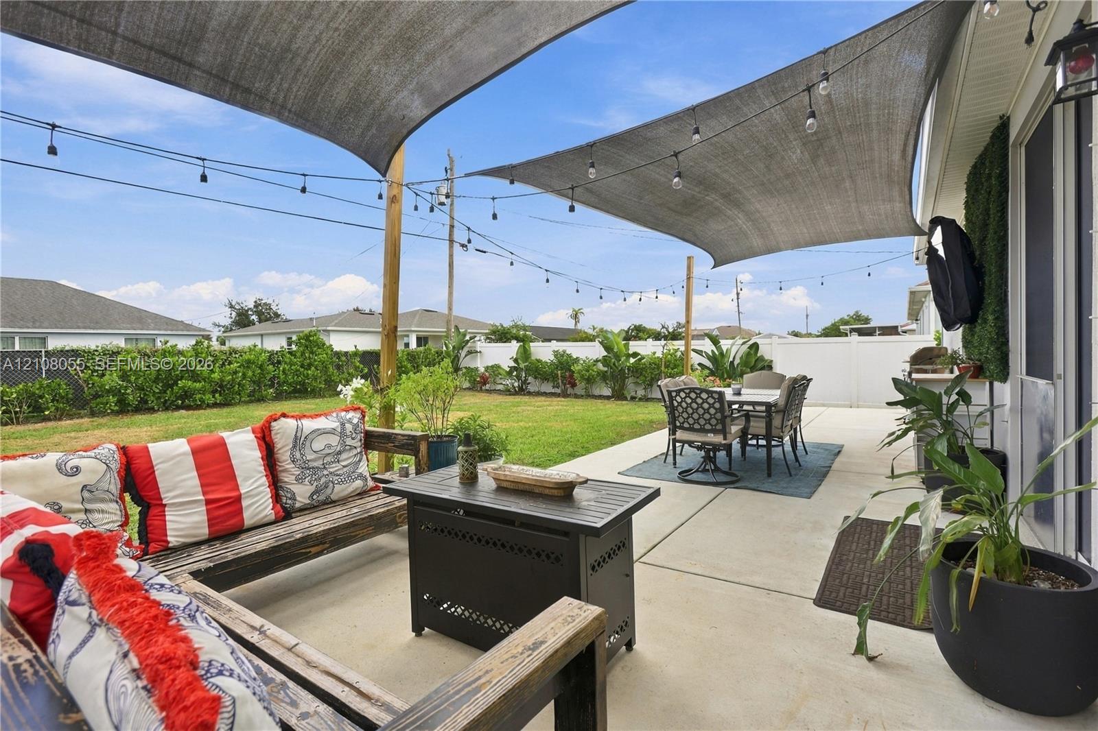 Concrete patio featuring a tension shade sail, overhead string lighting, perimeter privacy fencing, and a manicured grass lawn