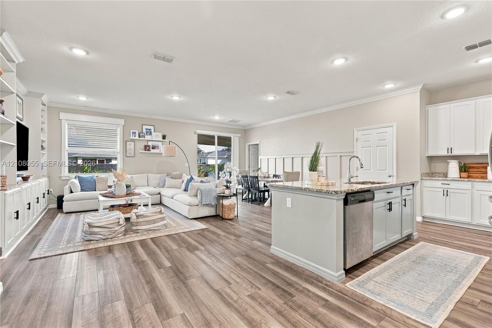 Open-concept area featuring wood-finish flooring, recessed lighting, built-in cabinetry, an island with a stone-finish countertop, and decorative wall paneling
