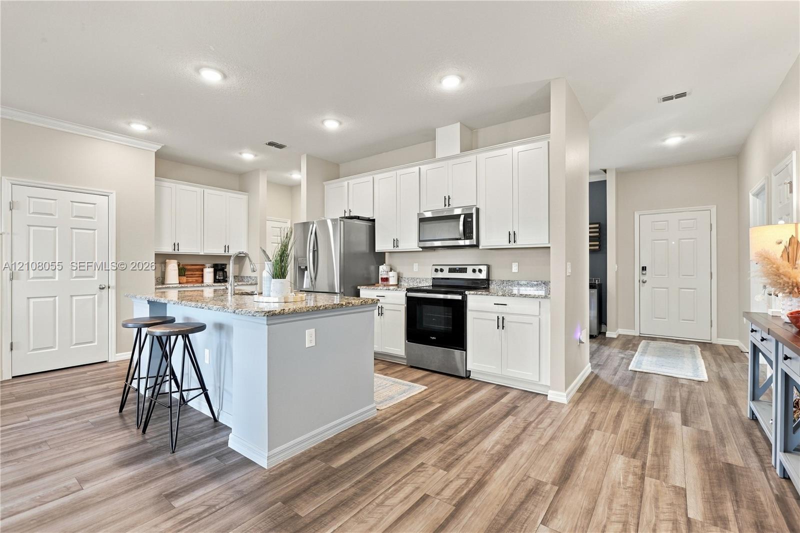 Kitchen featuring white cabinetry, stone-finish countertops, stainless steel appliances, a center island with sink, and wood-finish flooring