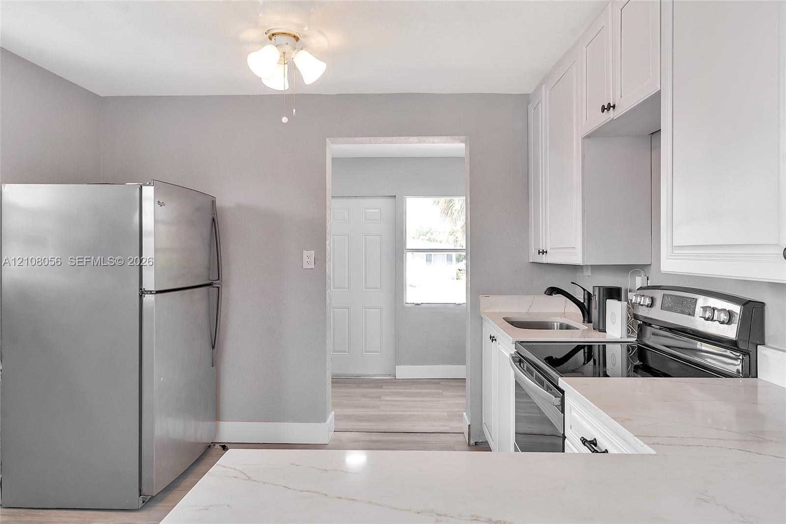 Kitchen featuring white shaker-style cabinetry, solid-surface countertops with grey veining, stainless steel refrigerator, stainless steel electric range, and matte black faucet
